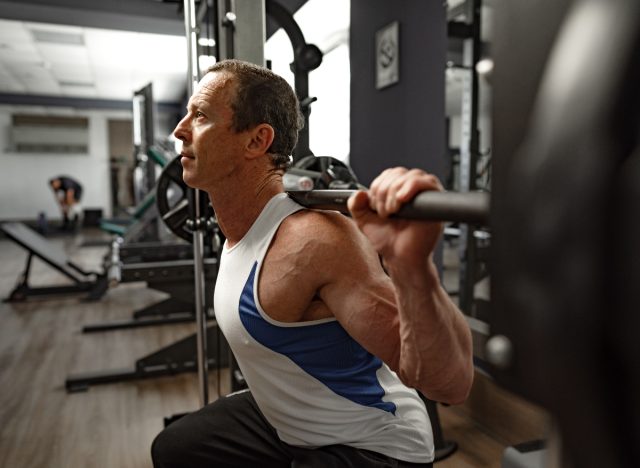 mature man doing barbell back squats