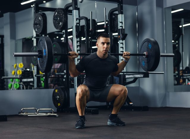 fit man doing barbell back squats at the gym