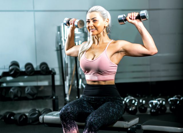 mogen, vältränad och stark kvinna som håller hantlar och spänner sina muskler på gymmet, koncept med övningar för överkroppsstyrka när du åldras