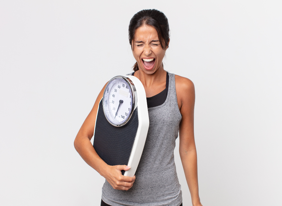 frustrated woman holding scale, concept of reasons you're not losing weight