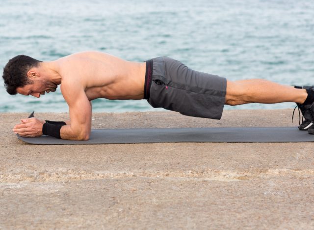 man gör underarmsplanka på yogamatta vid vatten, koncept med kroppsviktsövningar för att hålla vikten nere