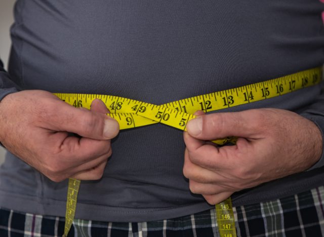 man measuring his waistline with tape measure