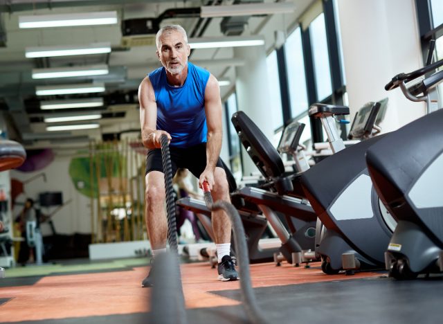 mature man doing battle ropes exercises at the gym