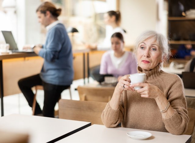 mature woman holding mug sitting alone in a cafe