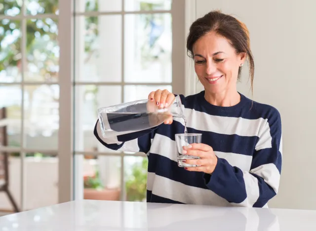 mogen kvinna häller ett glas vatten i sitt kök