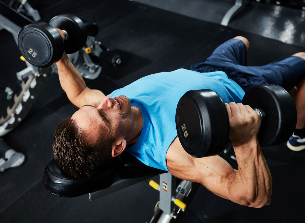 muscular man doing bench presses, concept of workouts for men to build muscle mass