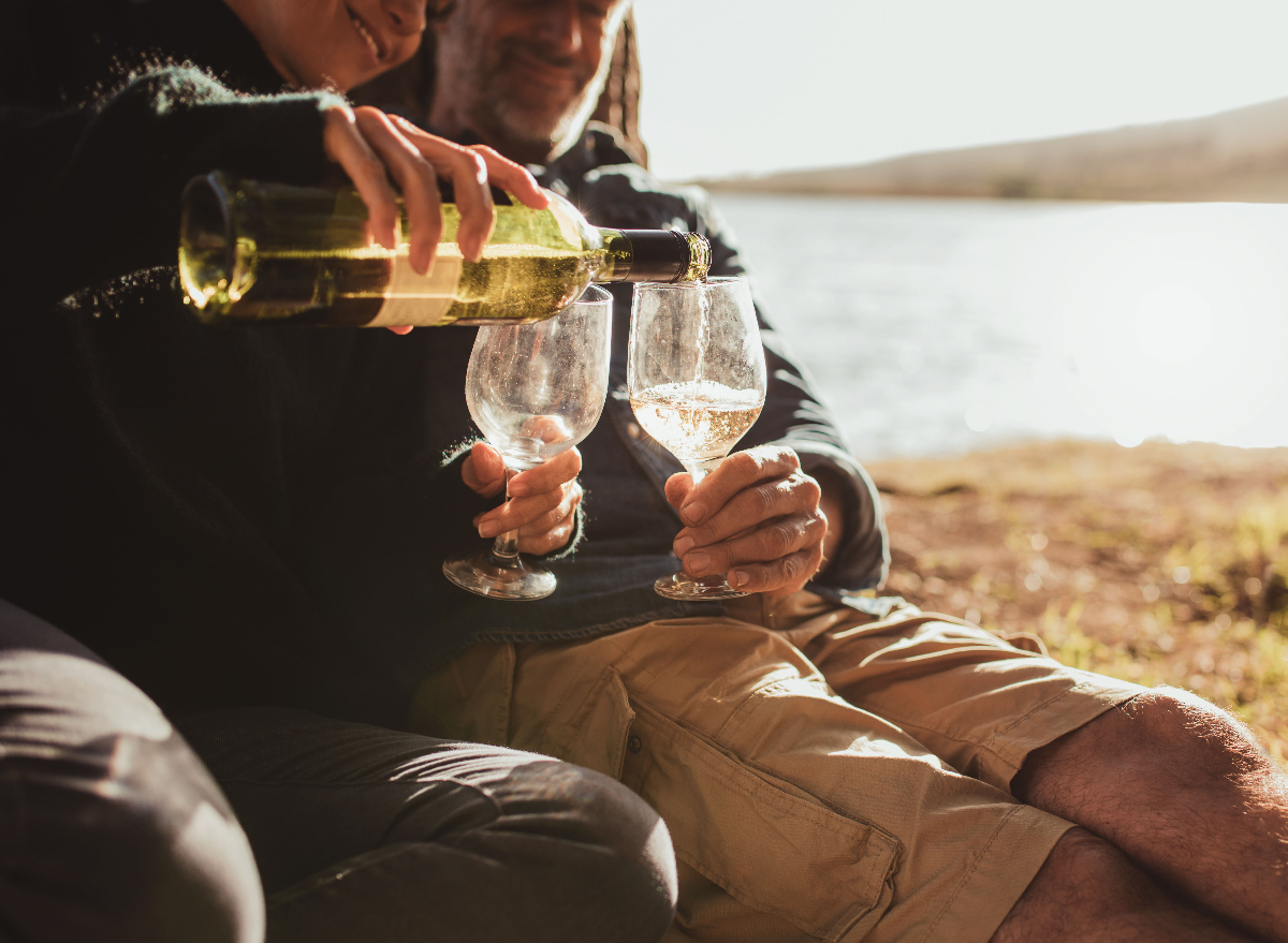 older couple pouring wine outdoors by lake, concept of worst habits for brain health