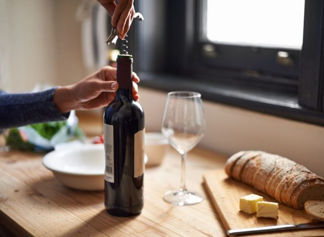 close-up hand opening wine bottle on table with bread, concept of alcohol being one of the worst habits for your brain