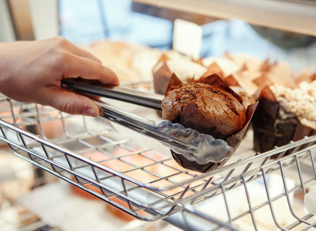 picking a muffin off the shelf with tongs at a bakery store