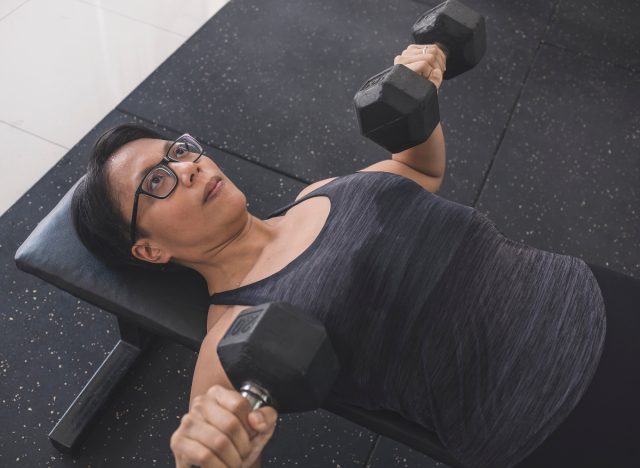 woman doing dumbbell chest press exercises for upper-body strength on workout bench