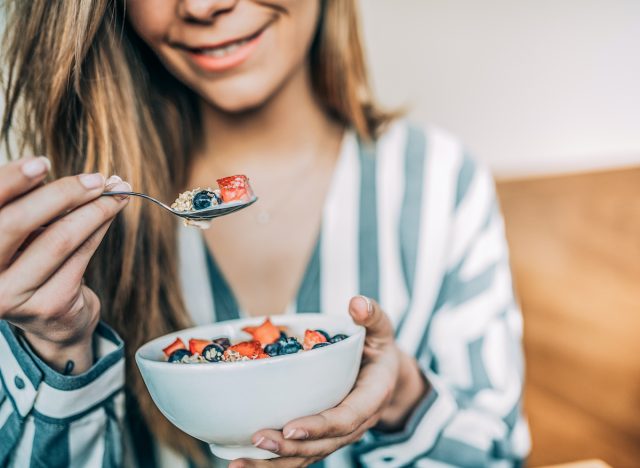 close-up woman holding bowl of oats and fruit, concept of breakfast habits to curb cravings and lose weight