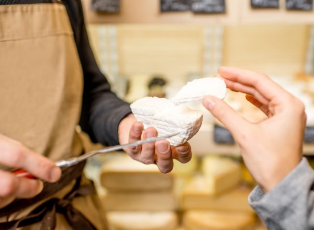 worker cutting a piece of cheese for a woman