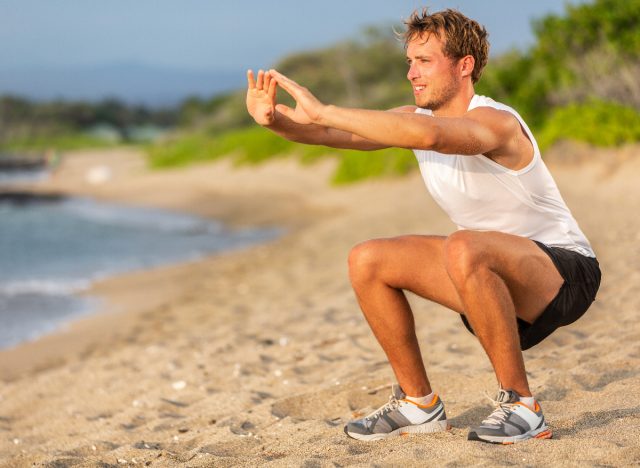 man doing bodyweight squats on a beach