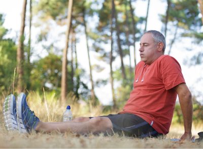man exhausted sitting down in grass after workout, concept of fitness habits to avoid to stay fit and healthy after 50