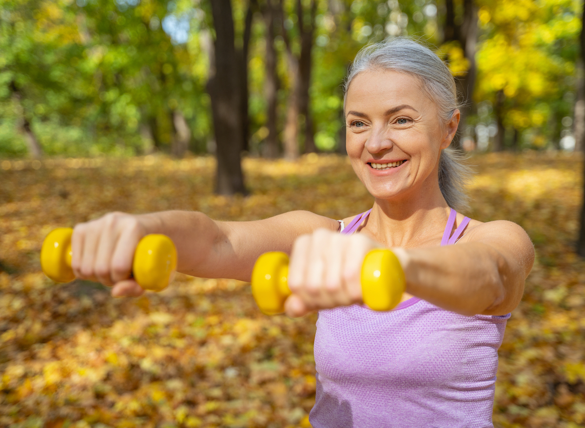 mature woman holding dumbbells outdoors, concept of daily arm exercises for women over 50