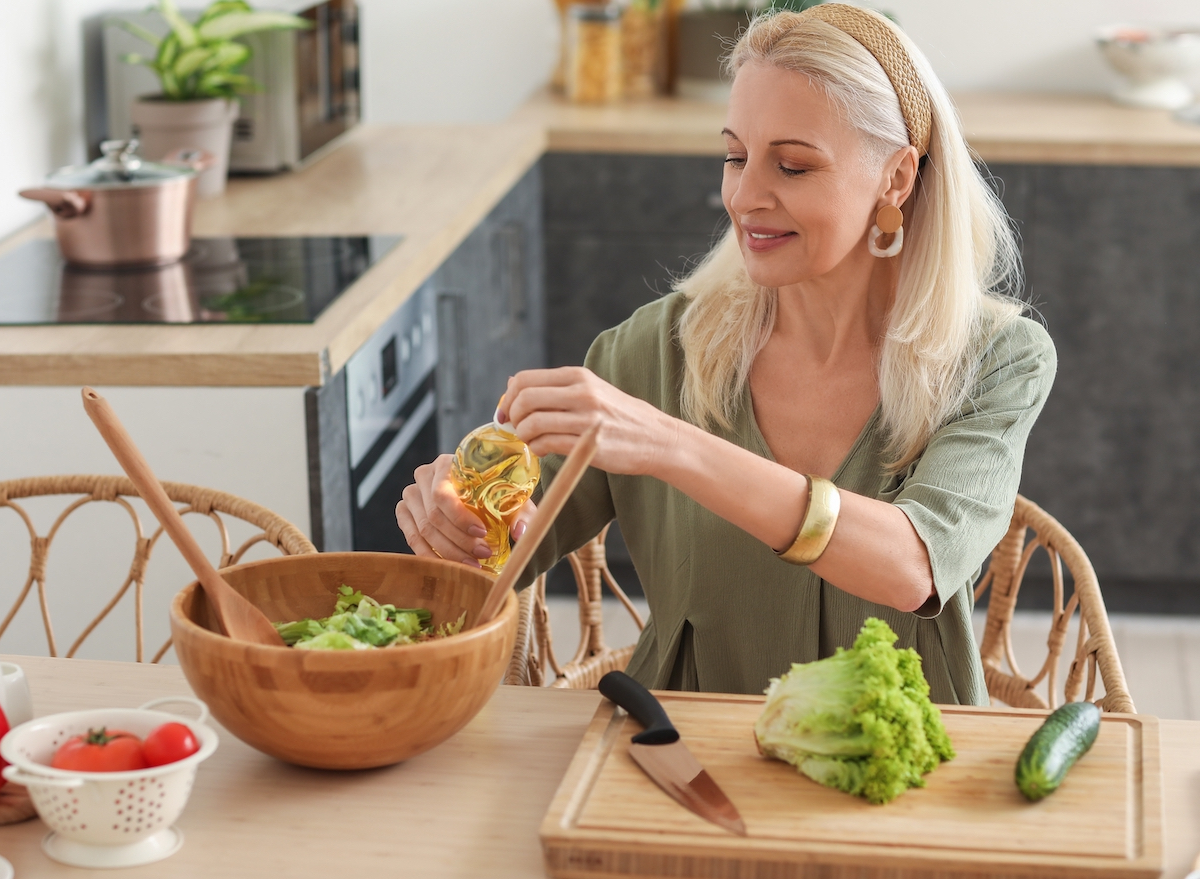 mature woman making fresh salad in kitchen, concept of daily habits for a slim waistline after 50