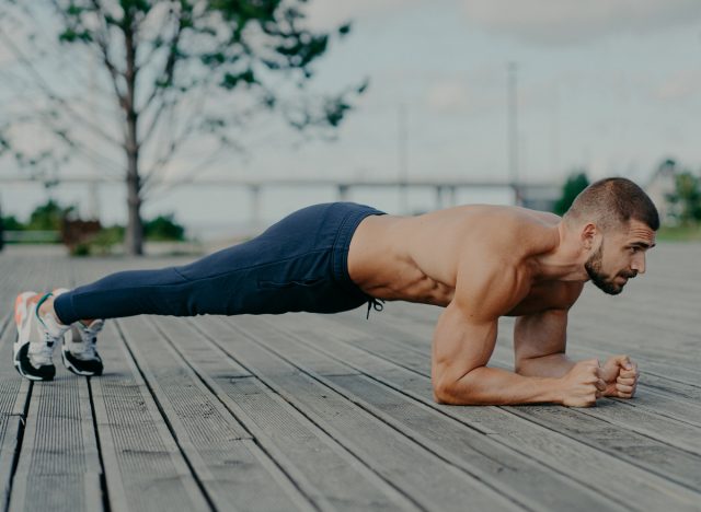 muscular man doing forearm plank outdoors, concept of daily exercises for men to get defined abs