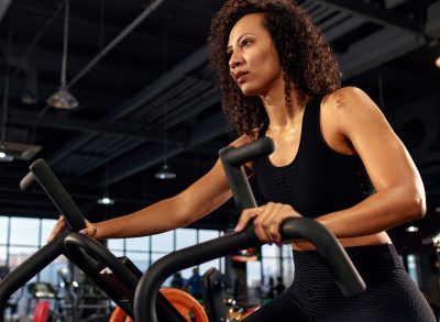 woman riding an air bike at the gym, concept of the best belly fat exercises to do at the gym