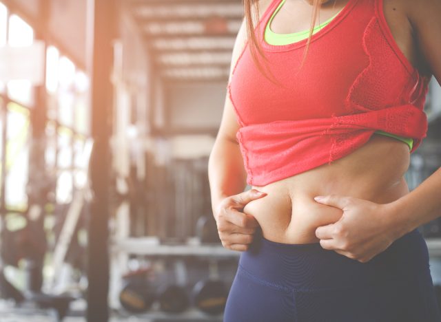 woman holding belly fat at the gym, concept of daily workout for women to melt hanging belly fat