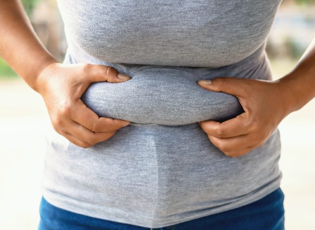 woman holding belly fat concept of habits that cause belly rolls