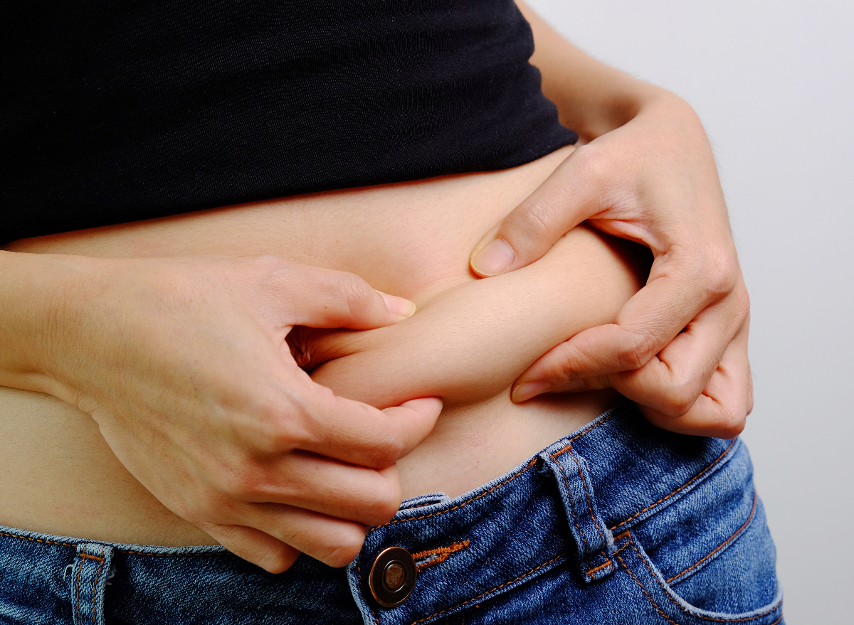 close-up woman pinching belly fat, concept of nighttime habits increasing belly fat