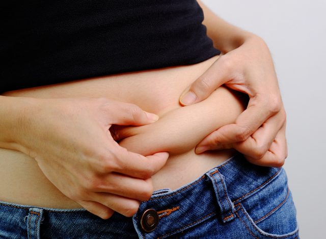 close-up woman pinching belly fat, concept of nighttime habits increasing belly fat