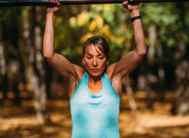 muscular woman doing pull-ups outdoors, concept of exercises to melt hanging belly fat in your 40s