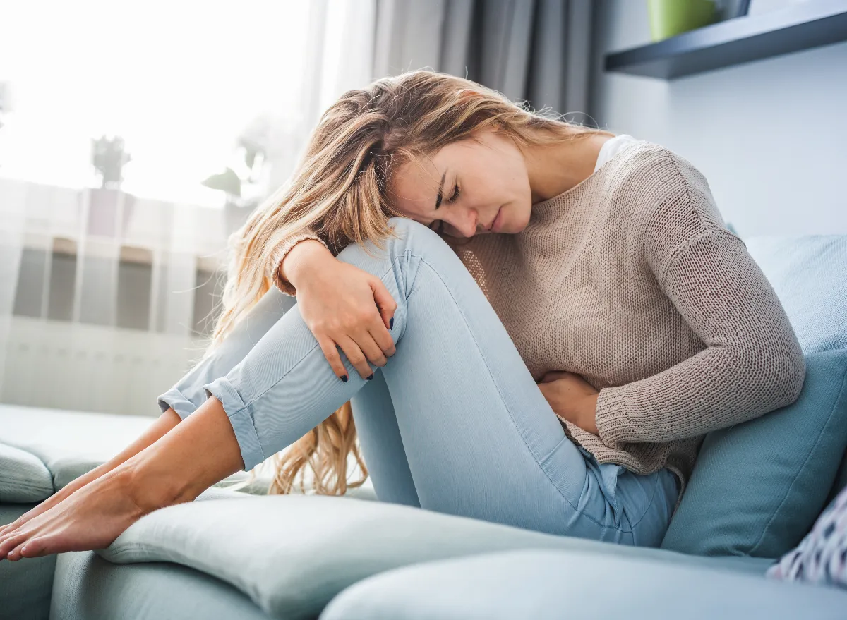 woman dealing with stomach cramps, constipation on couch, concept of reasons you can't poop