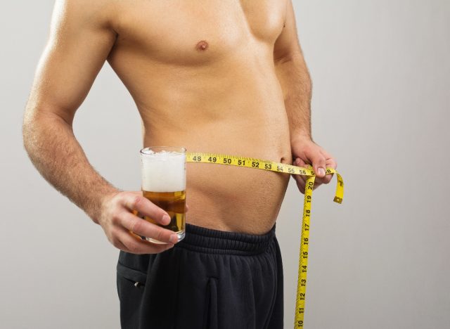 measuring beer belly and holding glass of beer, concept of how to get rid of your beer gut