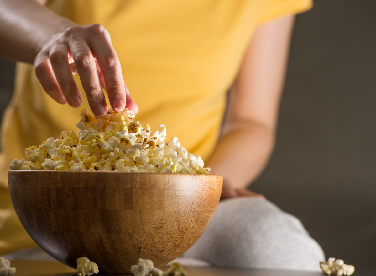 close-up woman's hand grabbing popcorn, concept of inflammatory foods that cause belly fat