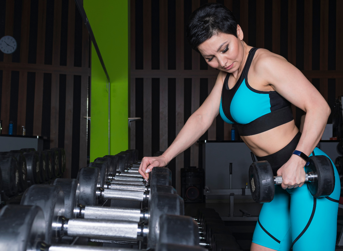 fit woman holding dumbbell next to weight rack at gym, concept of exercises to feel firm and fit after 40