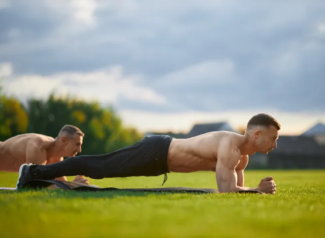 mature muscular man doing planks outdoors in group fitness class