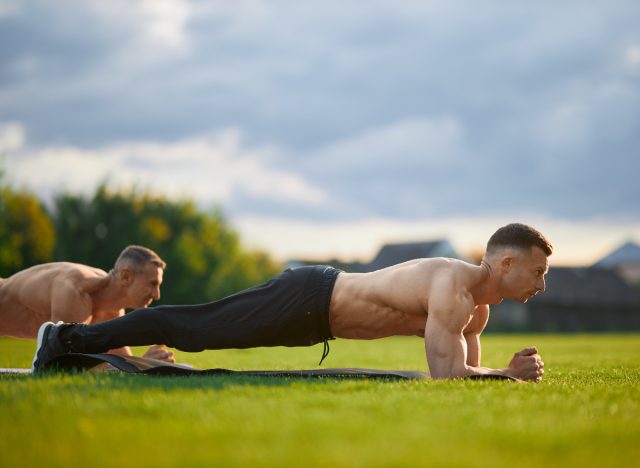 Strengthen Your Body With These 10 Exercises For Men' - mature muscular man doing planks outdoors in group fitness class