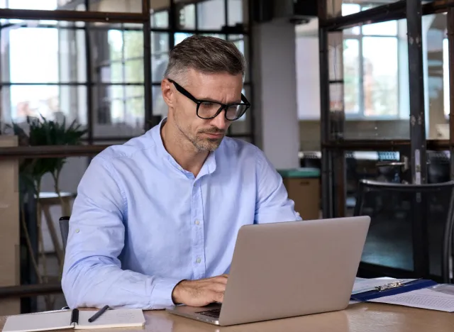 man typing on laptop at table, desk setup