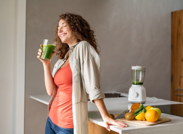 happy woman drinking green juice in kitchen, concept of tips to lose 20 pounds
