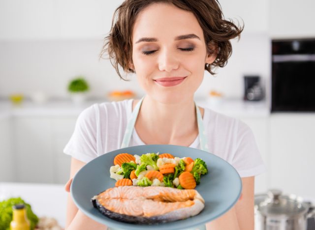woman holding healthy plate of salmon and veggies, concept of foods that stimulate brown fat for weight loss