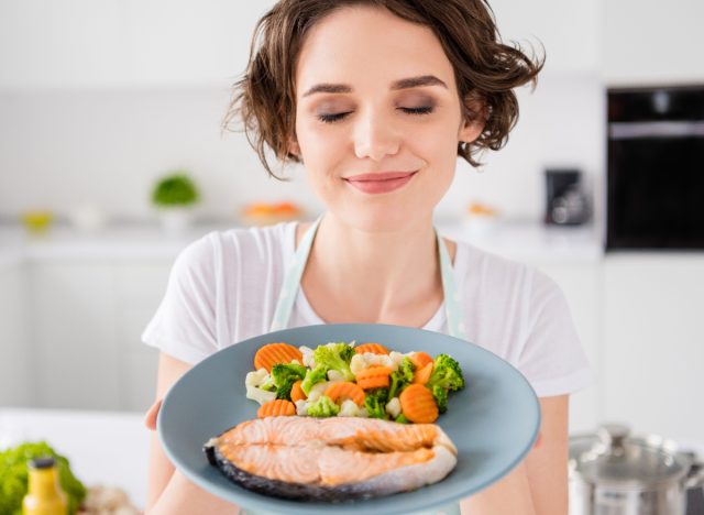 woman holding healthy plate of salmon and veggies, concept of foods that stimulate brown fat for weight loss