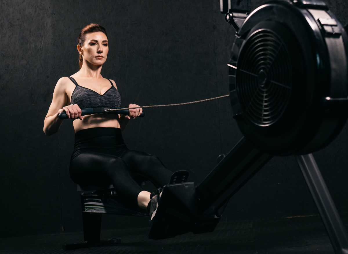 middle-aged woman using rowing machine, concept of exercises to shrink your waistline after 40