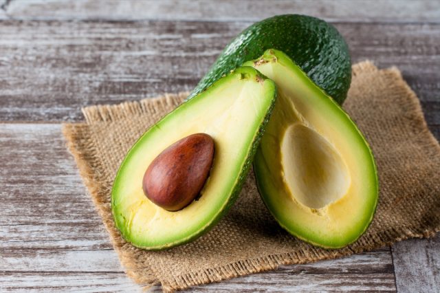 Close-up of an avocado and avocado oil on wooden table.