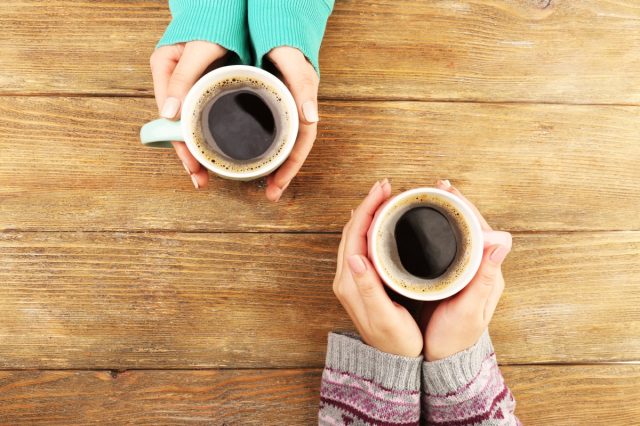 Female hands holding cups of coffee on rustic wooden table 