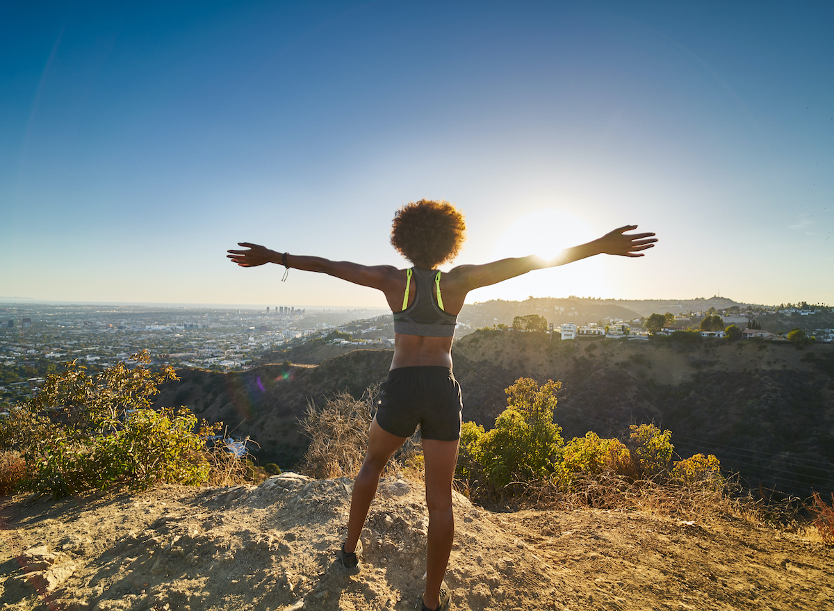 happy woman hiking at top of mountain, concept of science-backed ways to get lean and toned