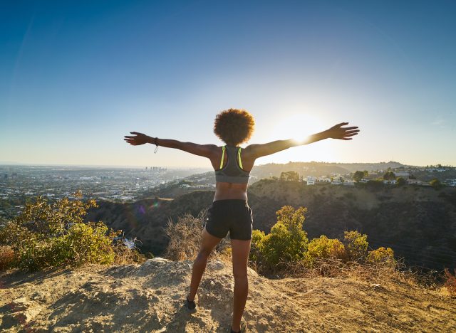 happy woman hiking at top of mountain, concept of science-backed ways to get lean and toned