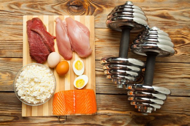 Protein diet, fish, cheese, eggs, meat, chicken and dumbbells on a wooden background