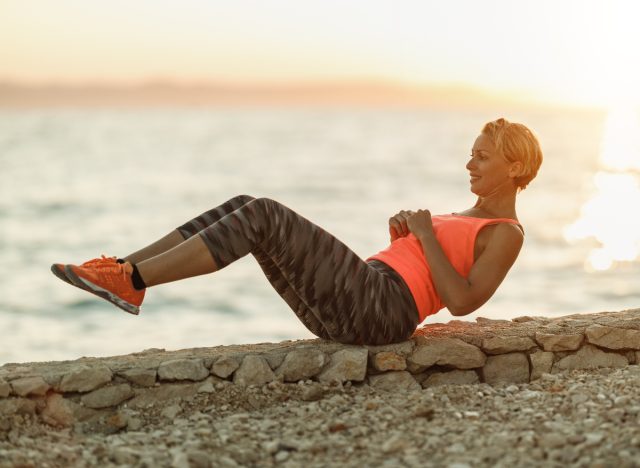 fit middle-aged woman doing core workout by the water, concept of workouts for flatter abs after 40