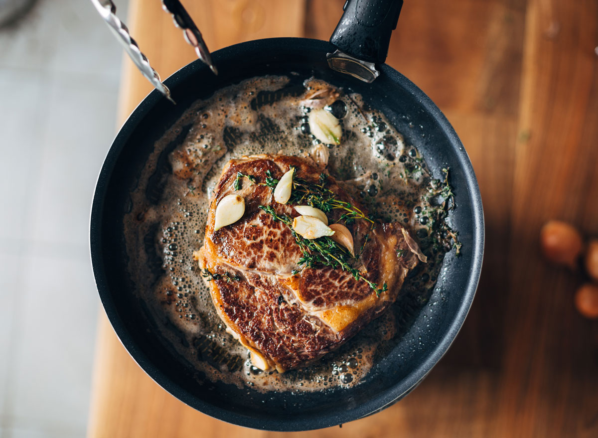 overhead cooking steak in a pan with butter and herbs