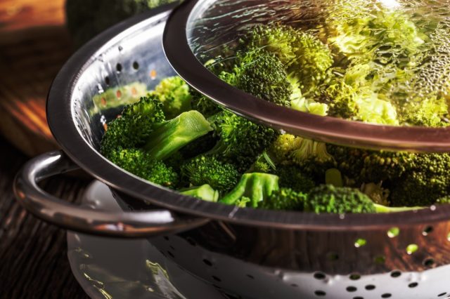Steamed broccoli in a stainless steel steamer with a lid