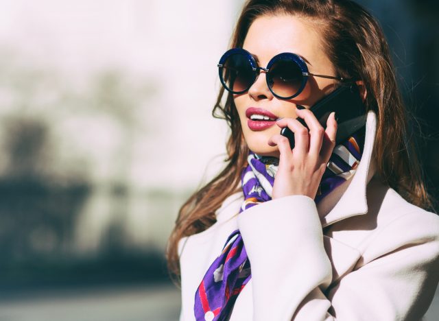 trendy woman talking on the phone wearing a scarf, peacoat, and sunnies