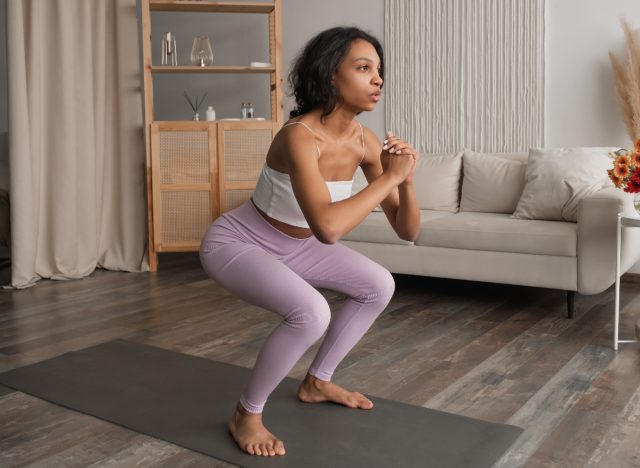 fitness woman doing bodyweight squats at home on yoga mat