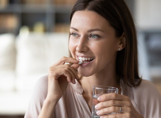 happy woman holding glass of water and taking vitamin, concept of best vitamins for women before 40