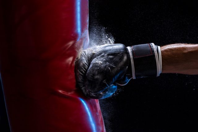 Close-up hand of boxer at the moment of impact on punching bag over black background